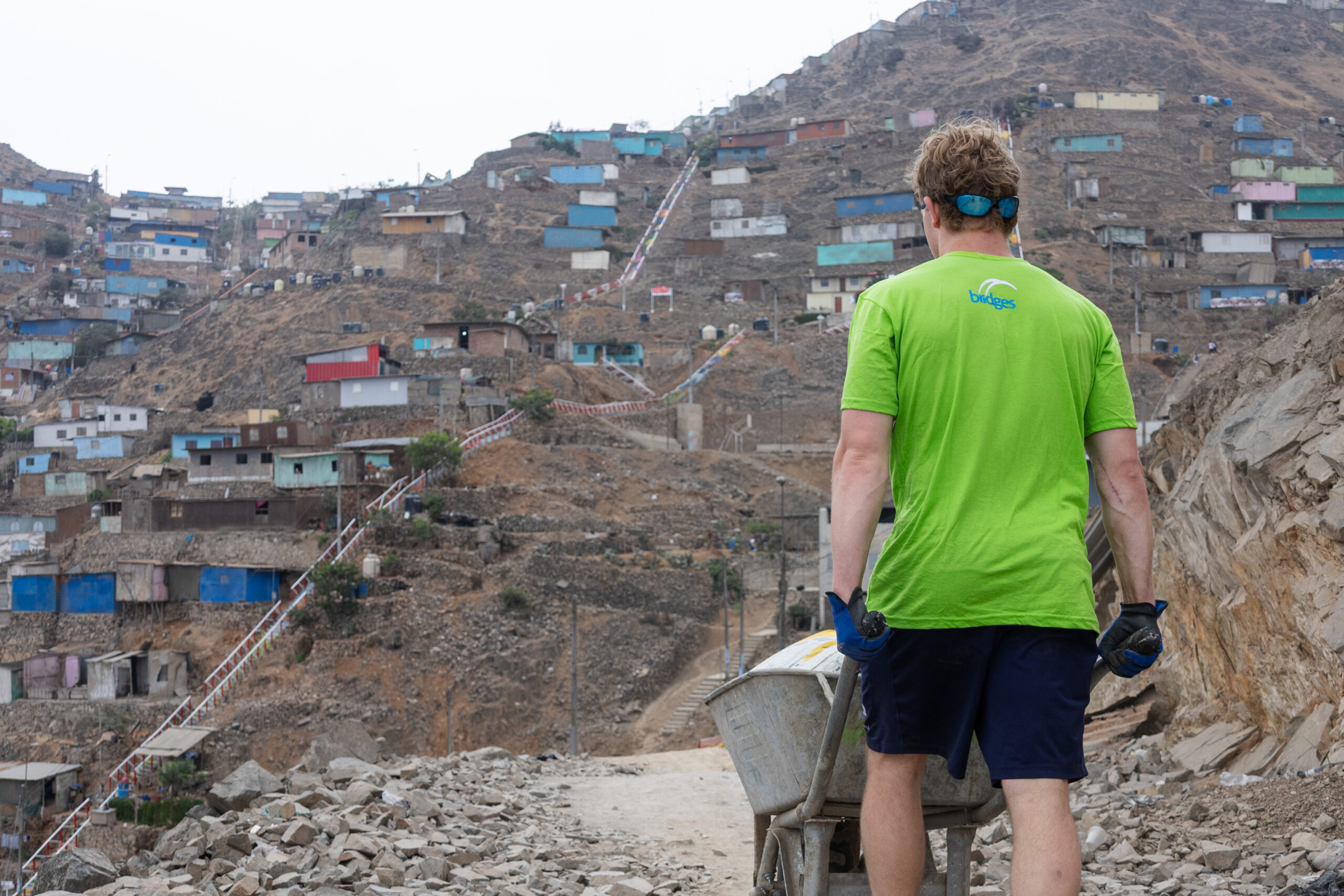 A Bridges volunteer with a wheelbarrow overlooking a hillside community